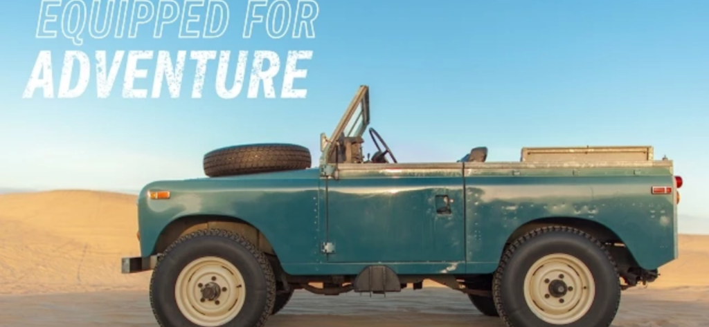 A topless Land Rover Series 3 on sand, with blue skies and the words 'Ready For Adventure' overlaid.