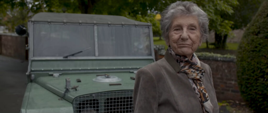 A lady called Dorothy Peters, proudly standing in front of a light green Land Rover Series 1