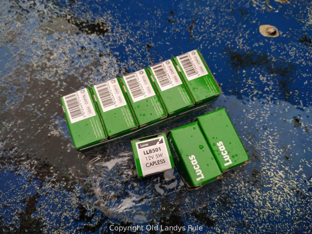 8 small green boxes, each containing a Lucas 12 volt 5 watt capless bulb - sku LLB501 - on a blue, grunge looking, background