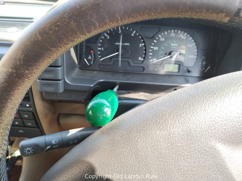 Looking through the steering wheel of a Discovery 2 at a green handled screw driver inserted into the left hand screw of the dashboard clock surround