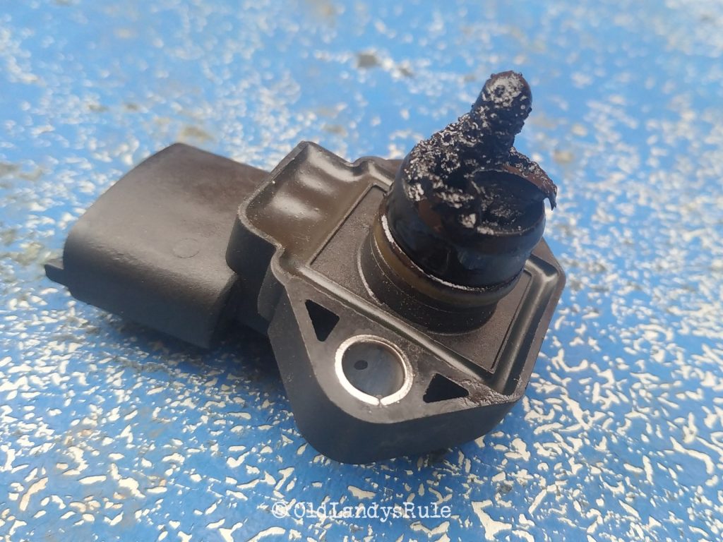 Close up of a Discovery 2 MAP sensor, all choked up in oil and grime, on a blue, grunge type, background