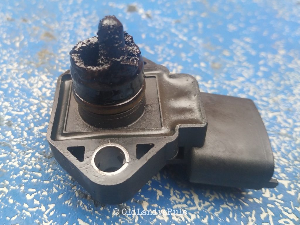 Close up of a Discovery 2 MAP sensor, all choked up in oil and grime, on a blue, grunge type, background