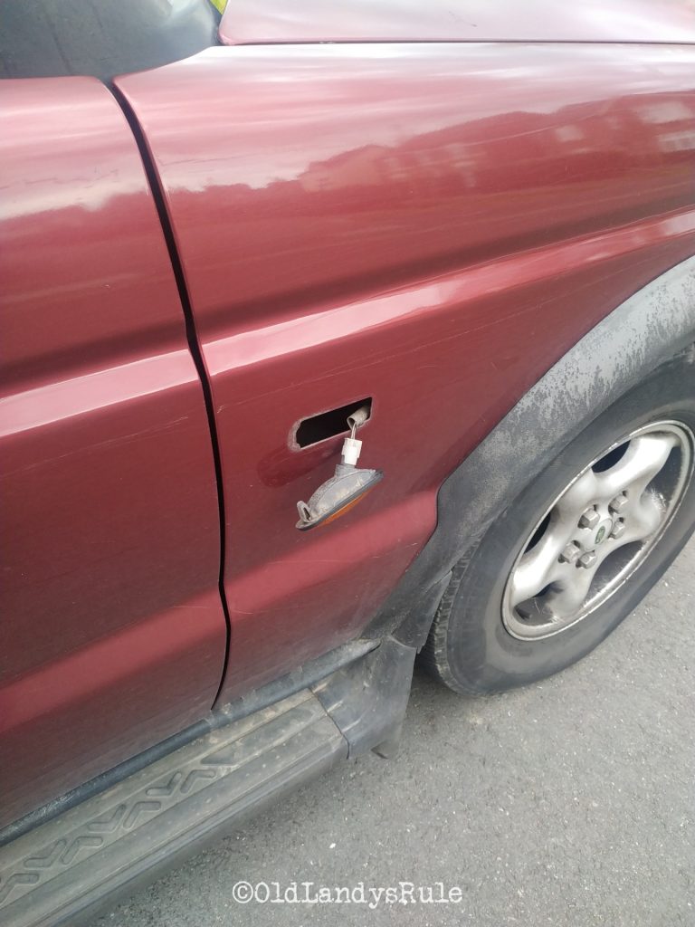 The indicator side repeater of a red Discovery 2, hanging out, still attached to the car by it's wires.