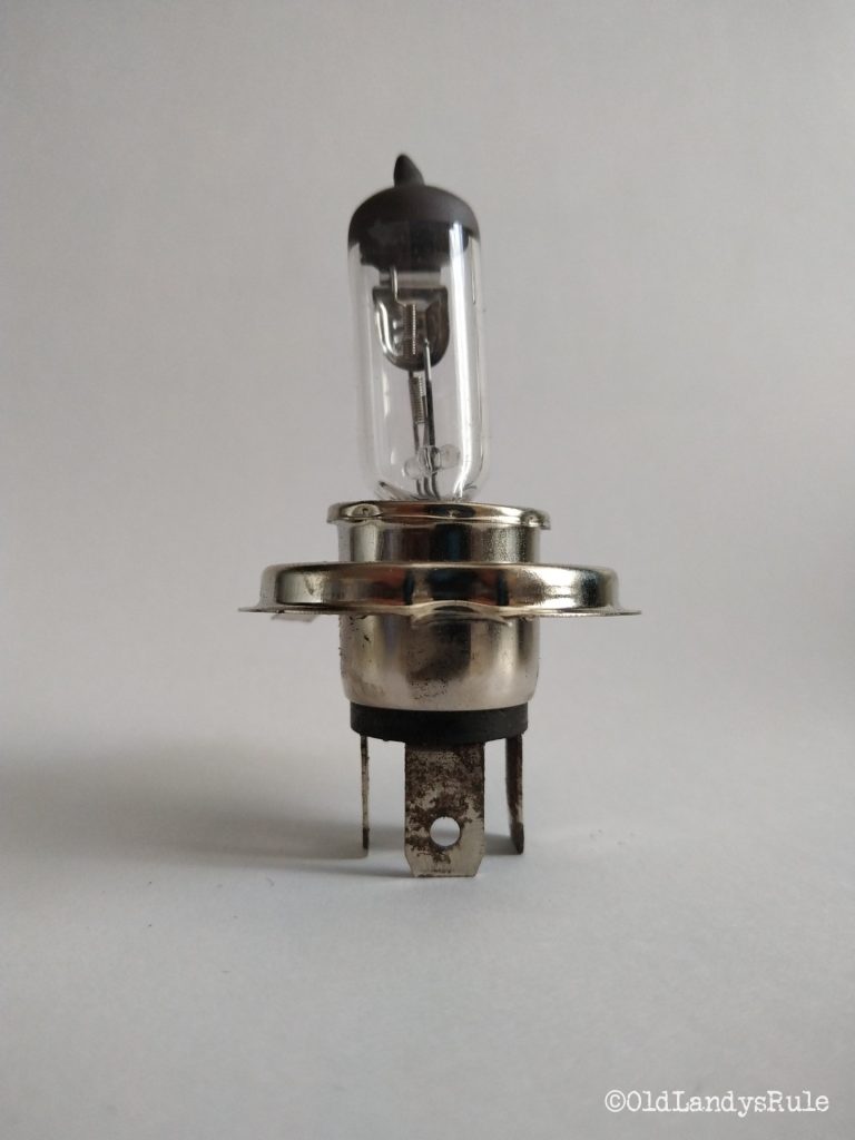 Closeup of a 3 pin connector headlamp bulb. The filament and glass case are leaning to the left indicating a manufacturing defect.