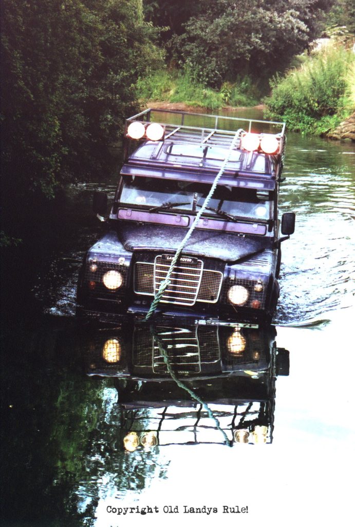 Land Rover Series 3, in blue, with a rope running from the front bumper over the roofrack to the rear of the car. There are 4 spotlights, switched on, mounted on the roof rack (like Camel Trophy vehicles). And the vehicle is in the middle of a ford with water over the front bumper. All the lights are on.