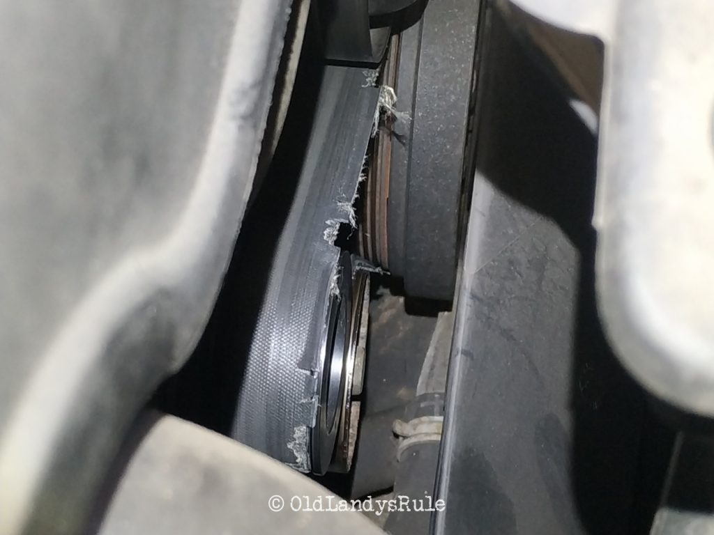 Close up showing a serpentine belt, of a Land Rover Discovery 2, and a pulley. The belt is frayed and damaged