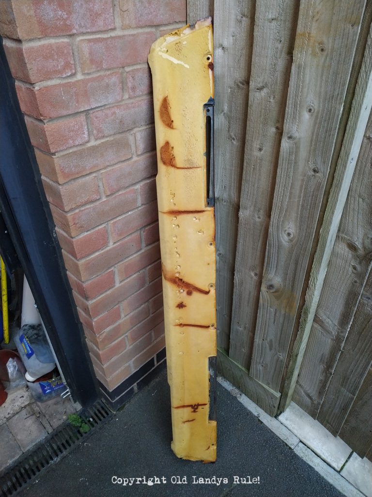 A Land Rover Series 3 dashboard top, stripped of its black vinyl so the foam is showing, leaning up against a brick wall, showing the sun damage cracks.