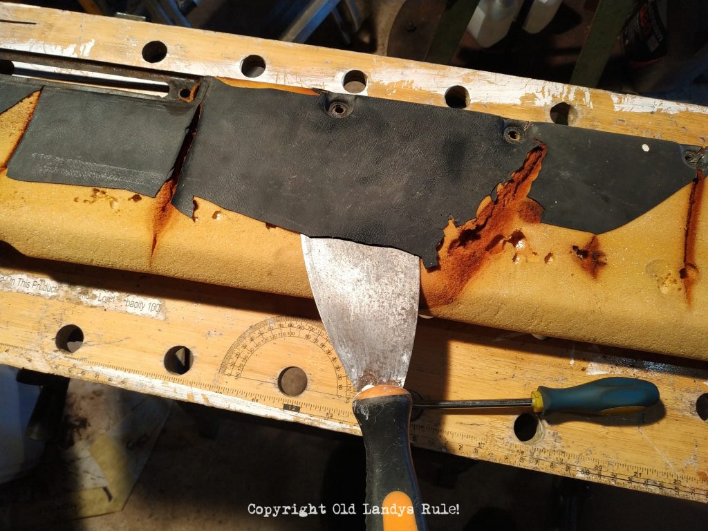 A wallpaper scraper, inserted under the black vinyl of a Land Rover Series 3 dashboard top, ready to peel the vinyl off