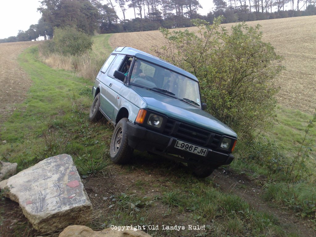 A blue Land Rover Discovery 1 on a greenlane, tilting violently to the left.