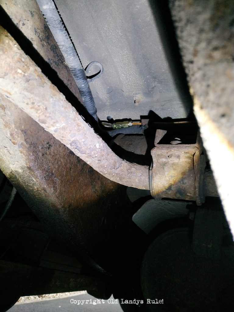 Underneath the rear of a Land Rover Discovery 2, looking up a brake pipe fitting running under the floor