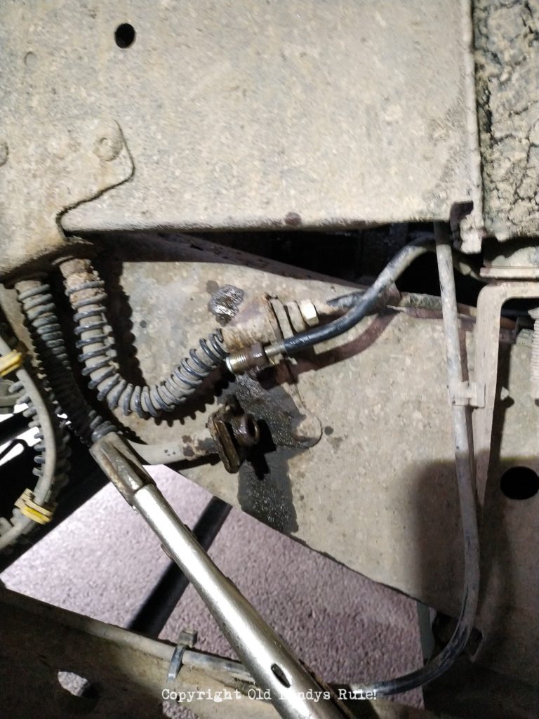 Close-up of a brake pipe that just been separated at the join with a flexi-hose. There is a pair of mole grips squeezing the flexi-hose. Another brake pipe and flexi-hose is visible just above.