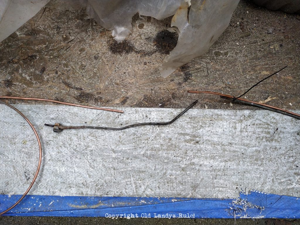 2 copper brake pipes, one of which is zip-tied to an old, rusty brake pipe, with a section of old rusty brake pipe just below.