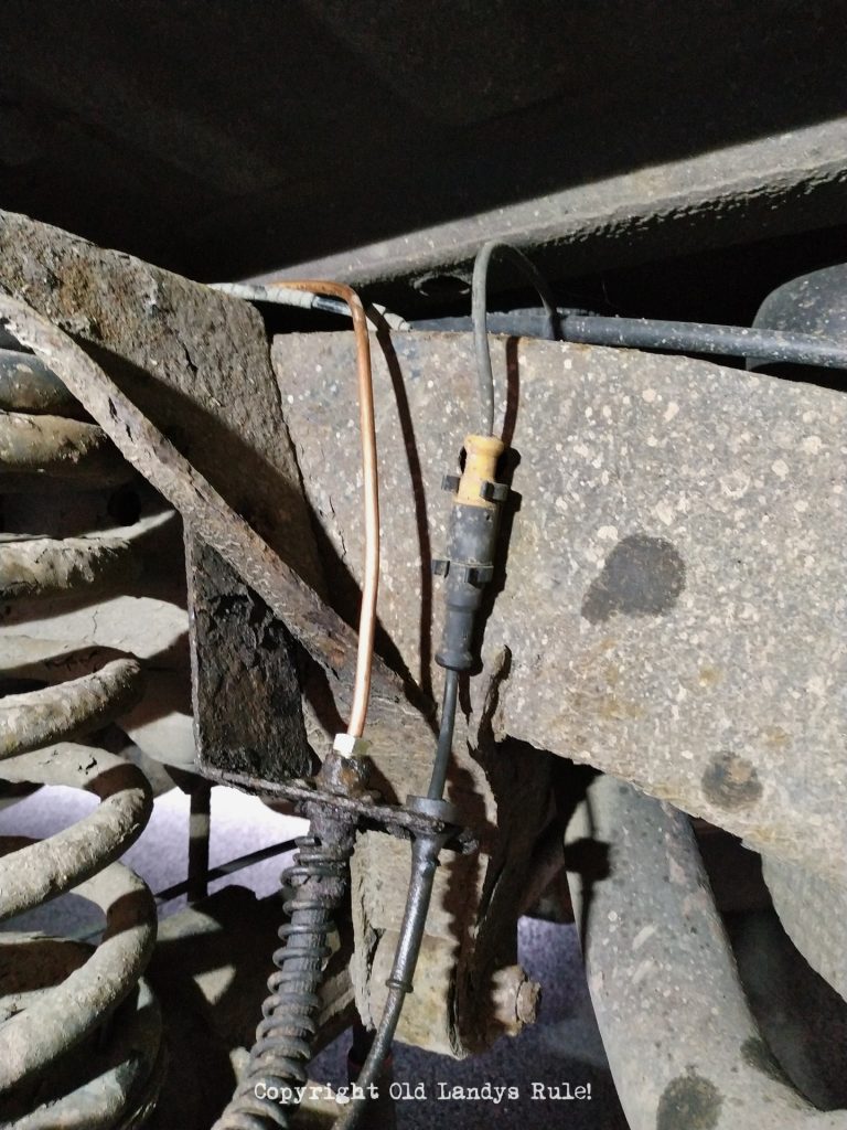 Close up of a new copper brake pipe joined to the old flexi-hose brake pipe. The brake pipe is copper and there is a suspension coil spring just visible to the left.