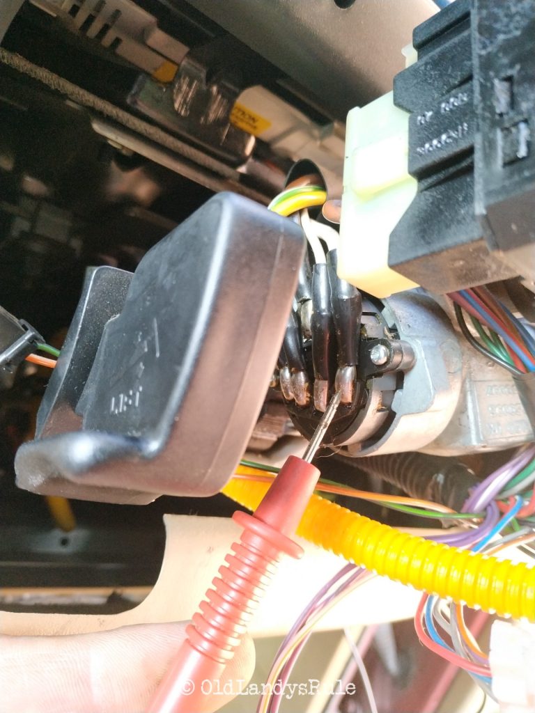 Closeup of a multimeter prove touching a wire inside a steering column