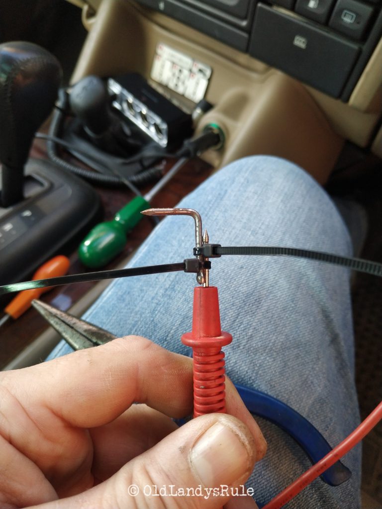 Closeup of a pin nail, bent at right angles, and zip tied onto the end of a multimeter probe.